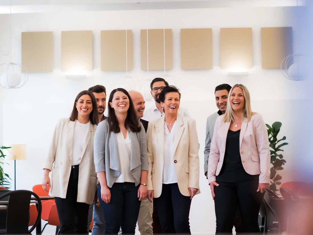 Bild von © Andi Bruckner: Eine Gruppe von ÖBV Versicherungsmitarbeiter:innen steht in einer modernen Büroumgebung und alle lachen glücklich in die Kamera.