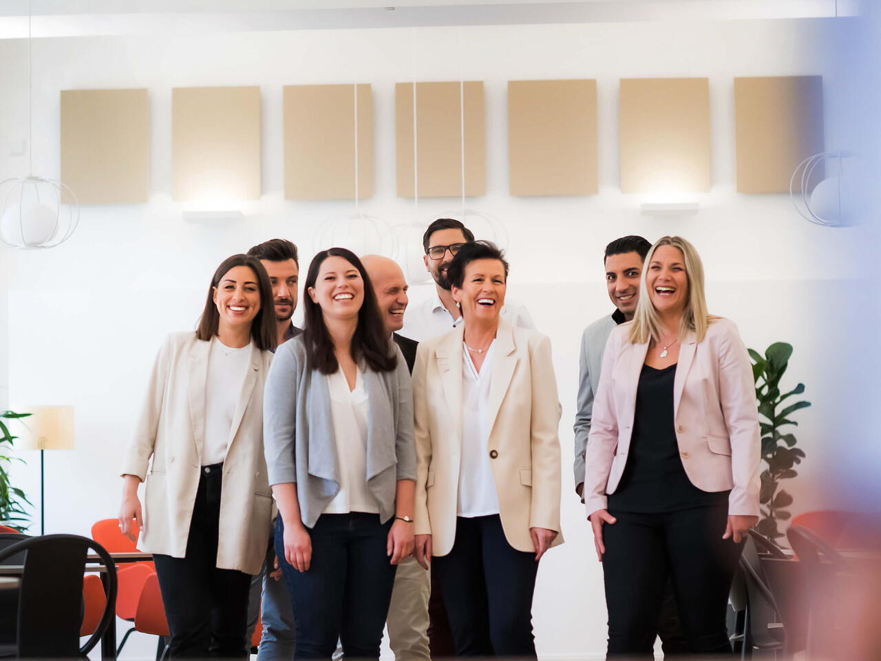 Bild von © Andi Bruckner: Eine Gruppe von ÖBV Versicherungsmitarbeiter:innen steht in einer modernen Büroumgebung und alle lachen glücklich in die Kamera.
