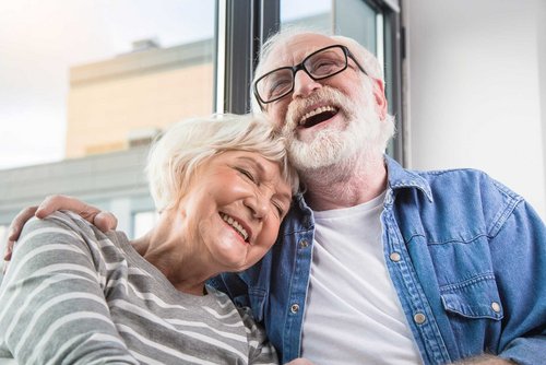 Ältere Frau und älterer Mann halten sich lachend im Arm.