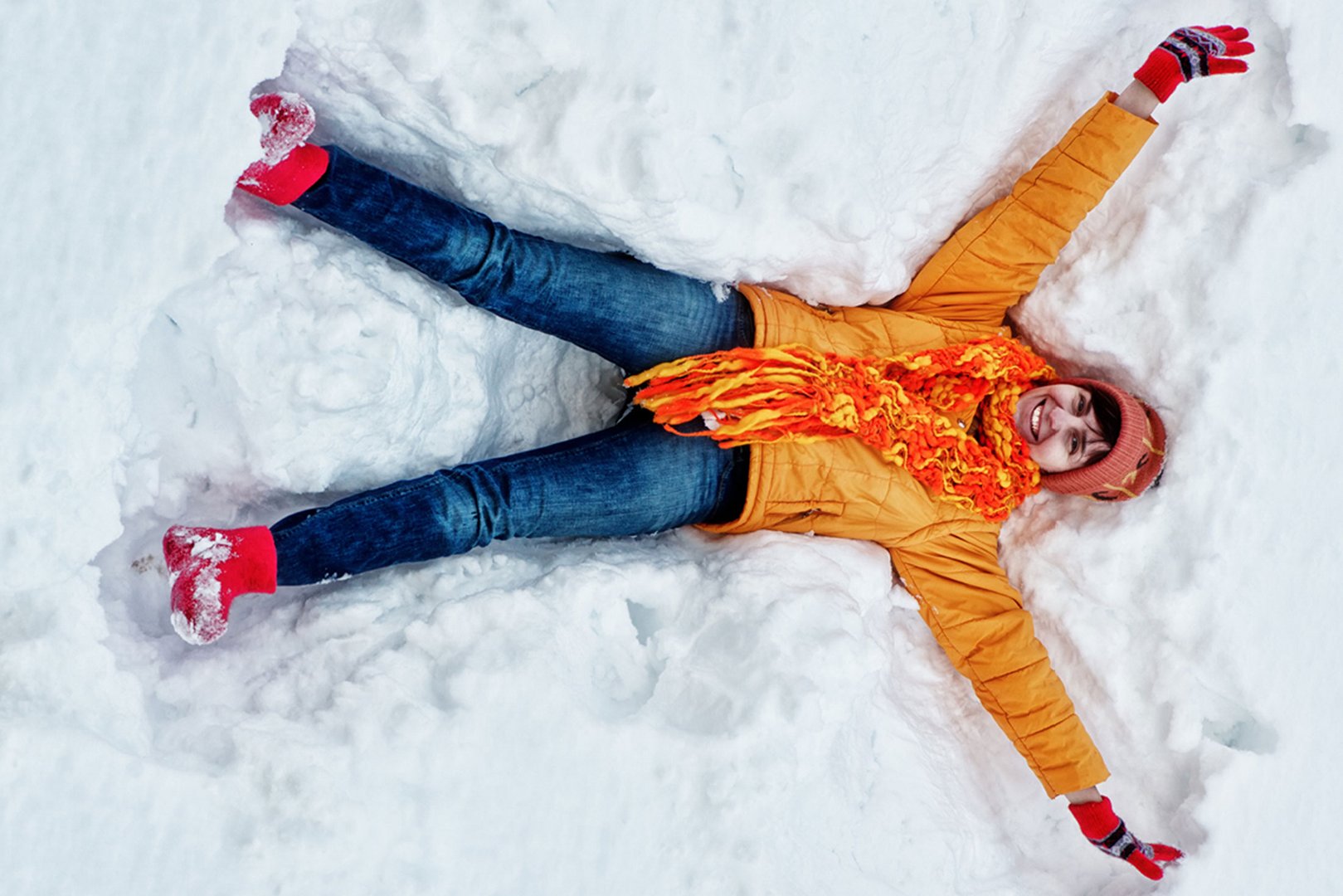 Frau mit oranger Winterjacke liegt im Schnee
