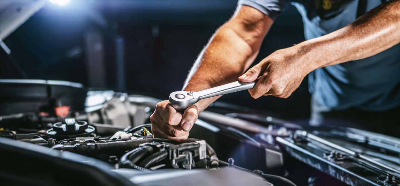 ÖBV KFZ-Versicherung Schadensfall Ein Mechaniker arbeitet in einer Werkstatt an einem beschädigten Auto.