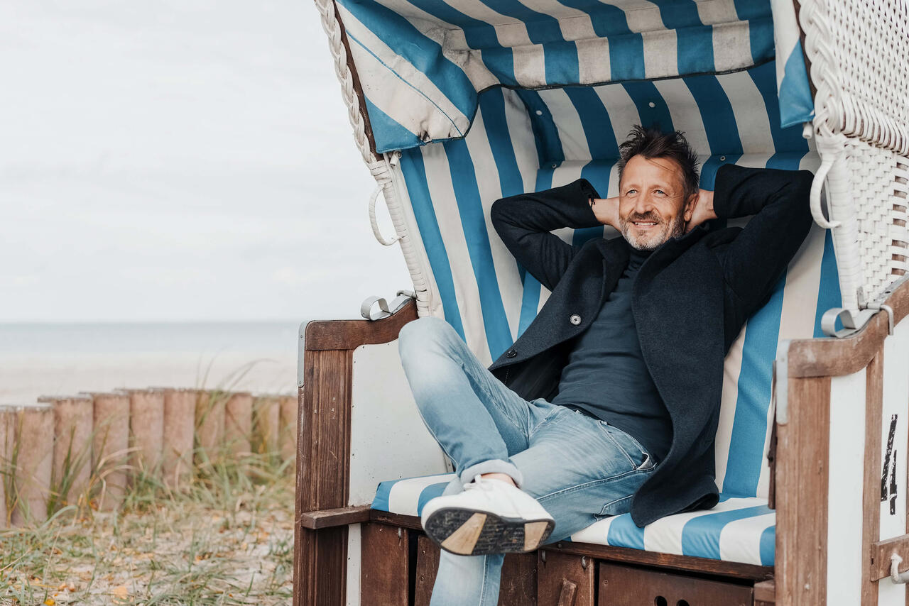 Auf alles vorbereitet sein: Ein Mann sitzt mit hinter dem Kopf verschränkten Armen in einem Strandkorb und lächelt zufrieden.