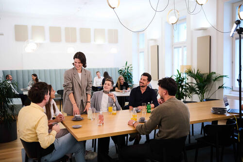 Eine Gruppe von ÖBV Versicherungsmitarbeiter:innen unterhalten sich fröhlich an einem großen Tisch.