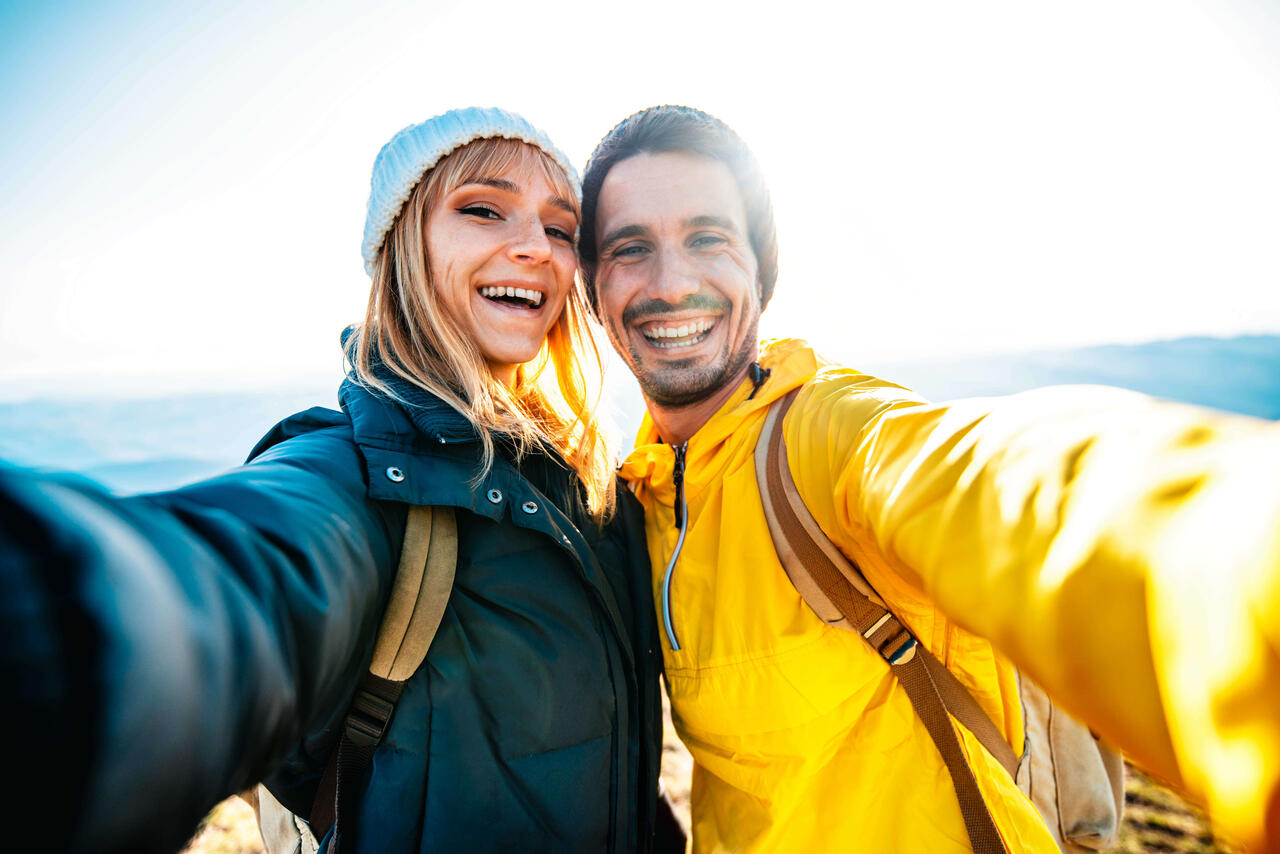Ein Pärchen ist draußen unterwegs, macht ein Selfie von sich und lächelt dabei glücklich in die Kamera