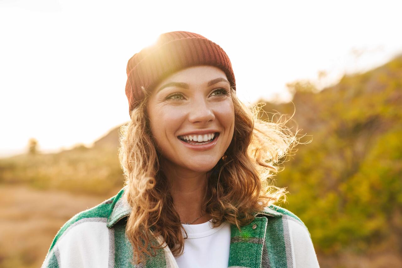 Eine junge Frau ist in der Natur unterwegs, wirkt sorgenfrei und lacht befreit.