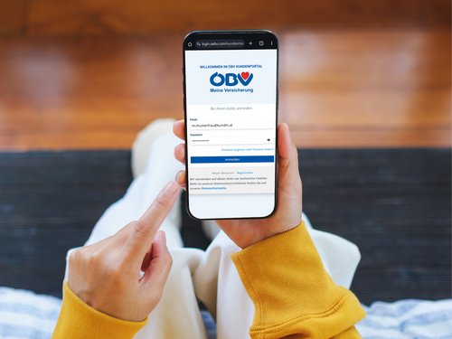 Eine Kundin der Österreichischen Beamtenversicherung hält ihr Smartphone in der Hand und loggt sich gerade ins ÖBV Kundenportal ein.