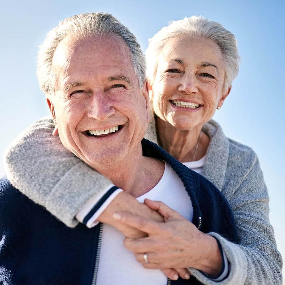 Lachende ältere Frau umarmt lachenden älteren Mann.