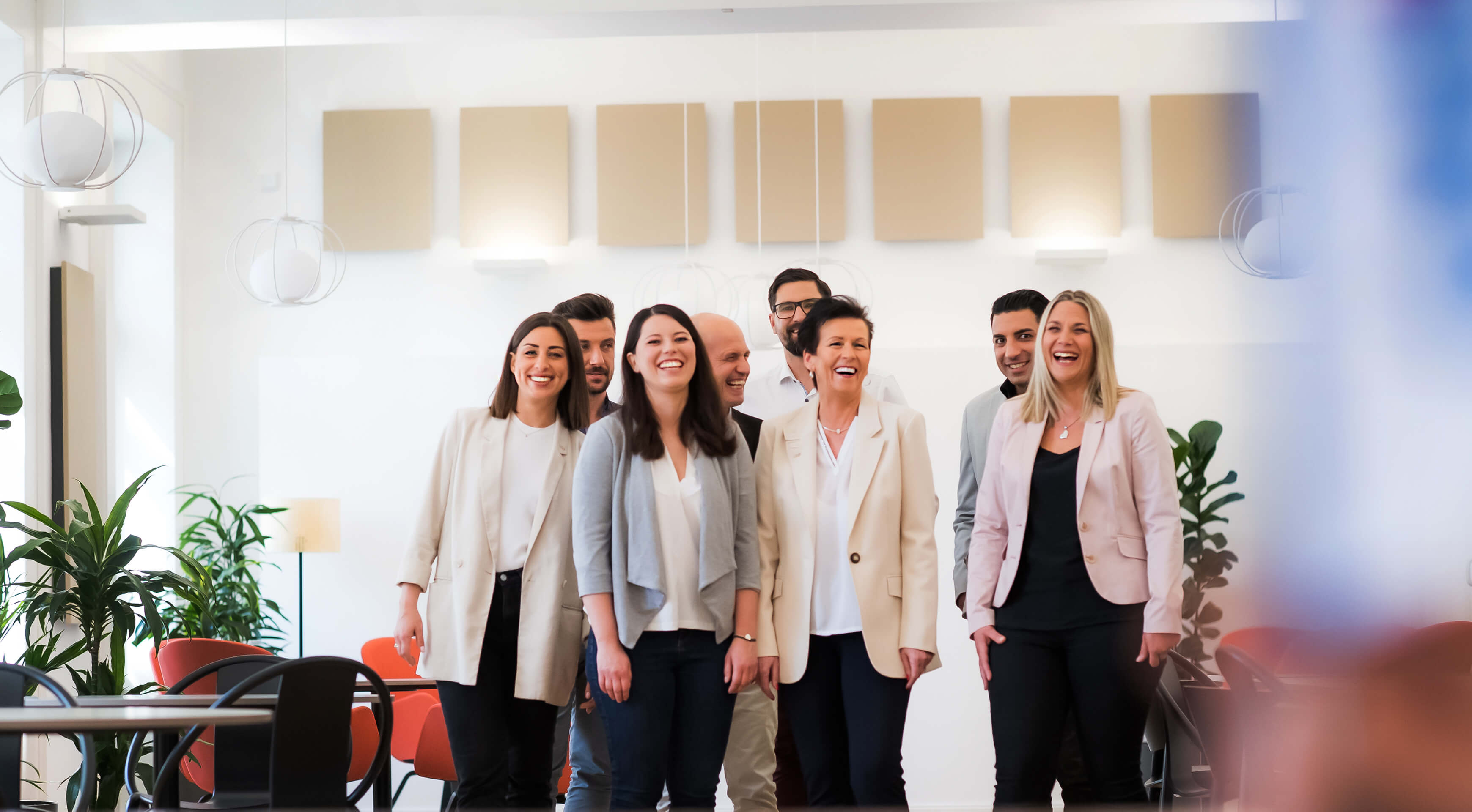 Bild von © Andi Bruckner: Eine Gruppe von ÖBV Versicherungsmitarbeiter:innen steht in einer modernen Büroumgebung und alle lachen glücklich in die Kamera.