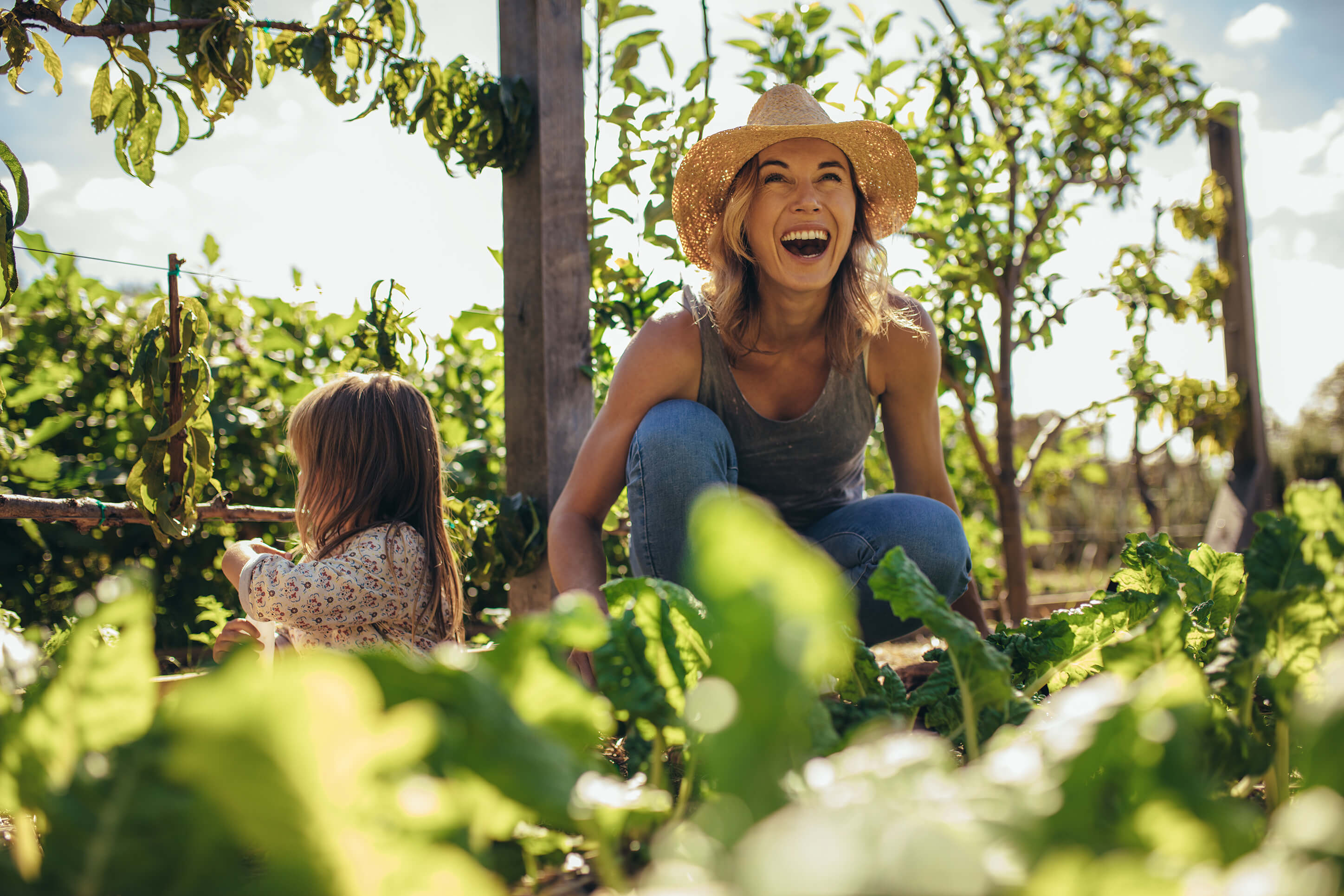 Flexibel und vielseitig: Eine Mutter ist mit ihrer Tochter im Garten. Sie trägt einen Strohhut und lacht.